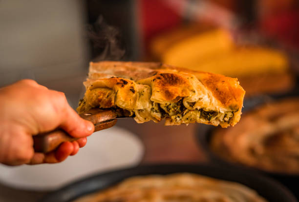 Close-up of a delicious, steaming spinach and cheese pie slice on a wooden spatula. The rustic background enhances the warm, comforting appeal of this freshly baked savory dish.