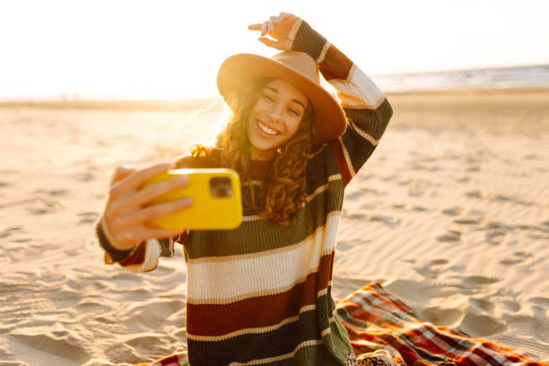 istock Young woman taking a cheerful selfie on a sandy beach during sunset. 2181523800