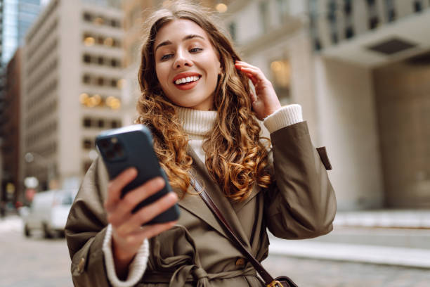 istock Stylish female browsing internet in smartphone while standing on street. 2181525044