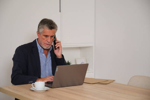 istock Senior businessman working from home and speaking on the phone while using laptop 2181529778