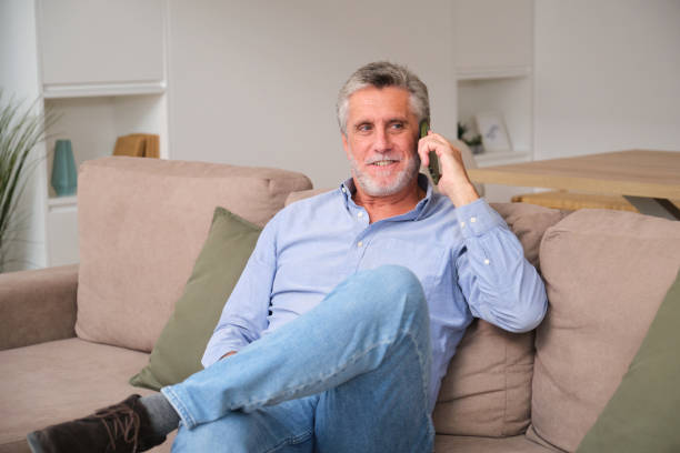 istock Senior man relaxing on sofa and talking on mobile phone at home 2181529813