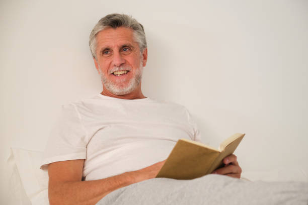 Young man reading book listening to headphone on white background