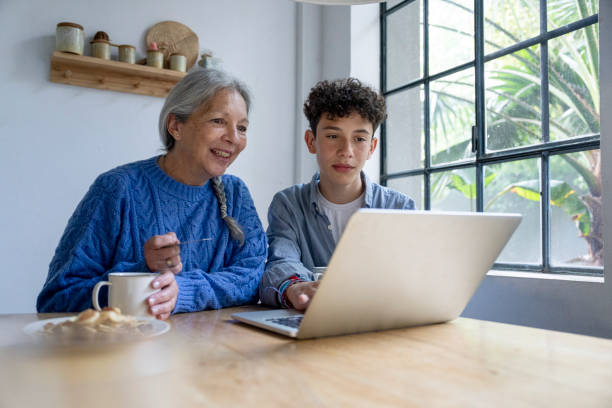 istock Young boy sitting in his grandmother's kitchen while helping her with her online Christmas shopping 2181531293