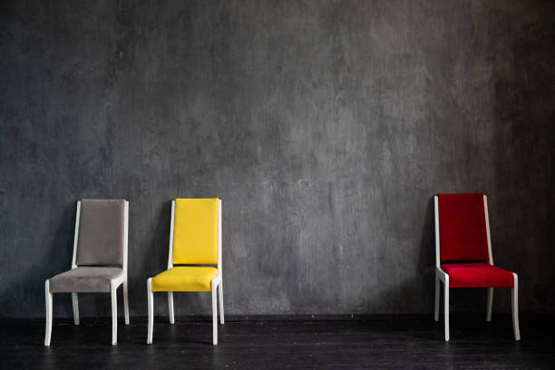 Five identical gray chairs stand in a symmetrical row against a textured concrete wall on a tiled floor. Clean lines and minimalist design create a sense of order and simplicity.