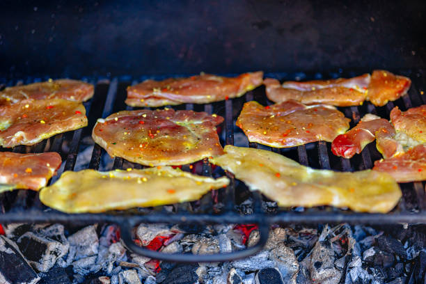 Marinated chicken strips are sizzling on a barbecue grill, surrounded by glowing charcoal, as friends enjoy a sunny outdoor gathering together.