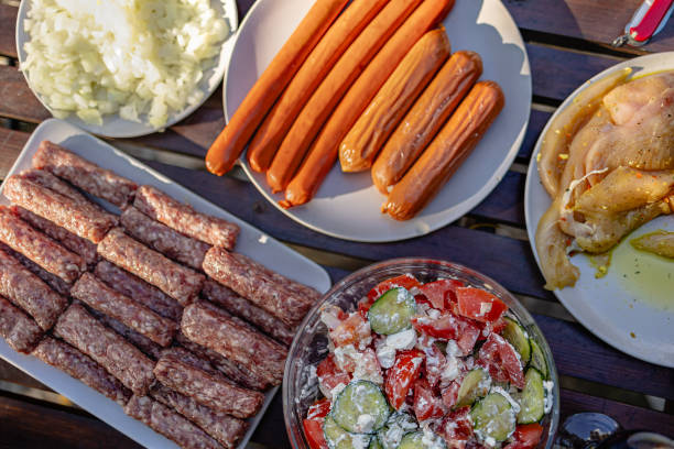 A vibrant barbecue spread shows an array of grilled meats, including sausages and chicken, accompanied by a fresh vegetable salad and diced onions, ready for outdoor enjoyment.