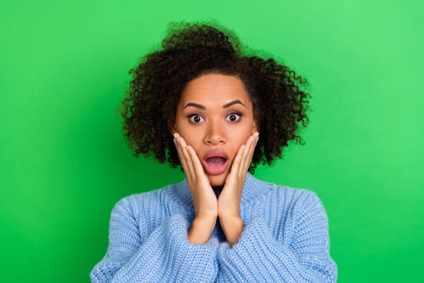 istock Photo of impressed curly haired girl dressed blue pullover palms cheekbones staring unbelievable sale isolated on green color background 2181539078