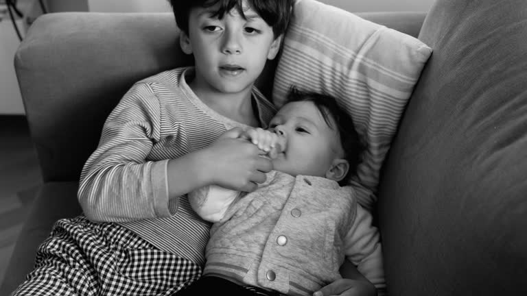 Older brother cuddling baby on the couch, peaceful moment of affection and connection, siblings lying together in a relaxed home setting, showing love and tenderness