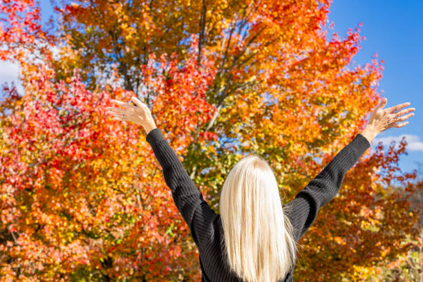 The back of a woman's head as she lifts her arms in excitement of the beautiful fall colors.