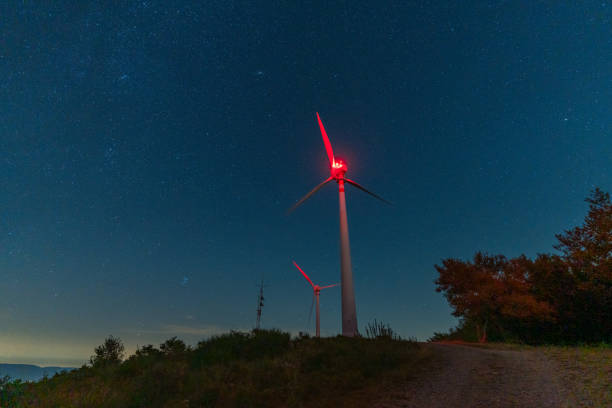Wind turbines with red warning lights rotating under a starry night sky, generating renewable energy
