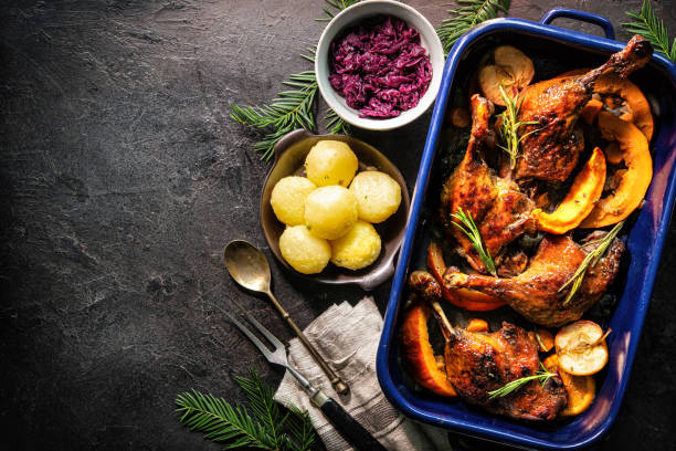Roasted duck legs in a roasting pan with dumplings and red cabbage.
