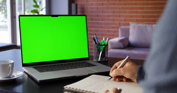istock Man Using Laptop Computer With A Chroma Key Green Screen In The Office And Taking Notes 2181572596