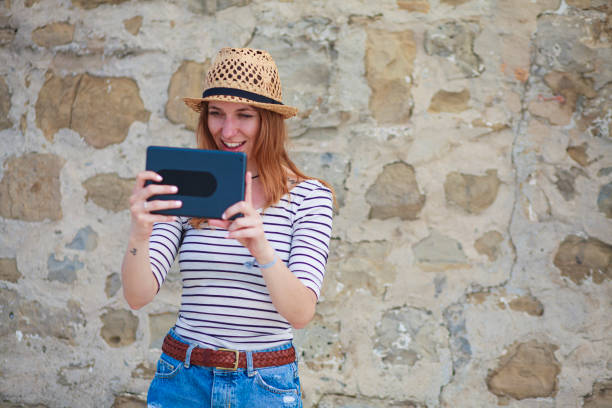 Cute young woman - photographer taking photos with  her digital tablet camera in front of an old stone wall.