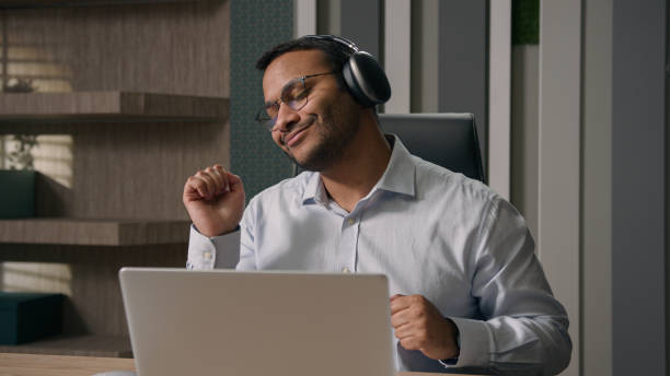 istock Happy employer at office table with computer laptop enjoying rest break dancing joyful Arabian Indian American businessman listening to music in headphones dance business worker man in office dance 2181575738