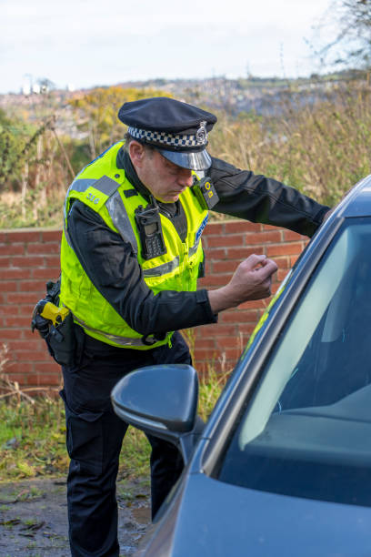 UK police officer approaching a parked car.  He is knocking on the side window to get the driver's attention.