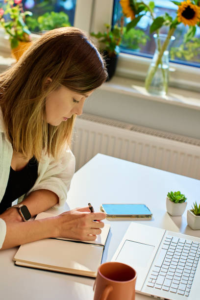 istock Woman working at home, writing in notebook and using laptop 2181580992