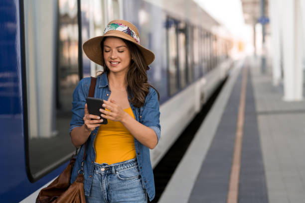 istock Young woman using phone while leaving a train on railway station. 2181589971