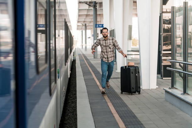Young man catching a train on railway station. Worried man running on train station while catching a train and going on a trip. running to catch the train stock pictures, royalty-free photos & images