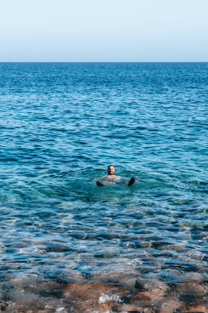A man is swimming in turquoise ocean. The water is clear and calm. The sky is blue and there are no clouds