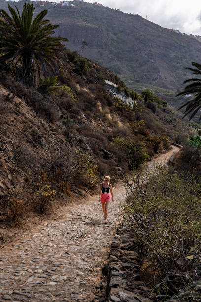 istock A woman walks along a rocky trail surrounded by lush greenery on a hillside 2181592611