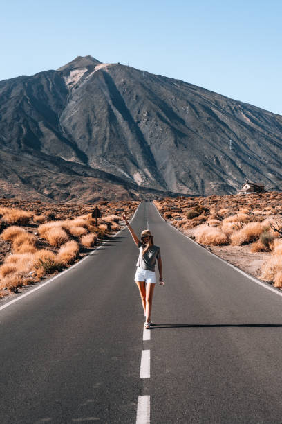 istock Woman walks along a deserted road with a mountain Teide background 2181592790
