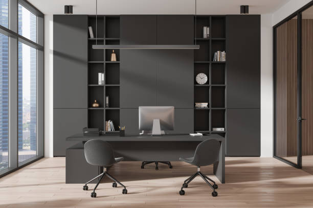 istock Dark business interior with work desk and pc, shelf near panoramic window 2181594546