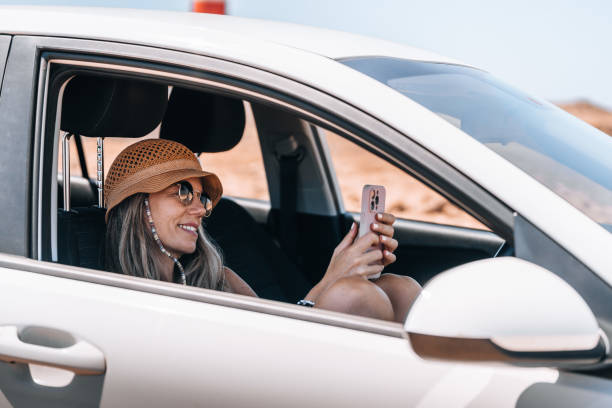 istock Woman with hat smiles while using her smartphone in a parked car 2181597176