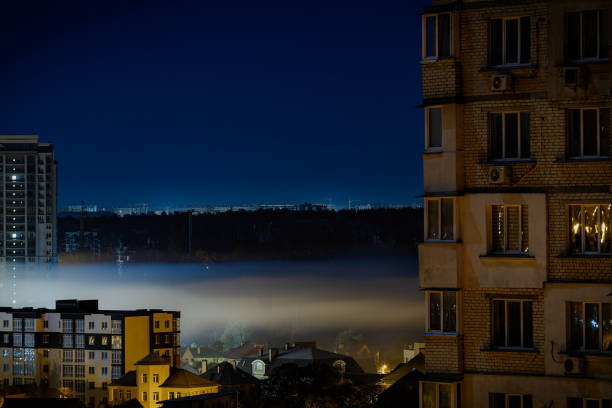 Night cityscape with thick fog. Clear weather, dense forest in the background