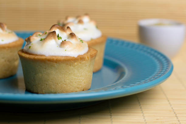 Images of small lemon tarts with white meringue cream with lemon zest and crispy crust, with blue plate, wood tones, very tasty, tasty dessert