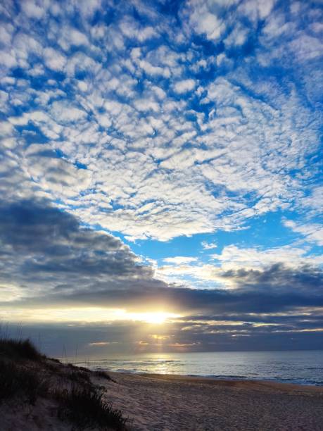 istock A stunning beach scene at sunrise with a dramatic sky filled with textured clouds, casting golden light over the calm ocean and sandy shore 2181609040