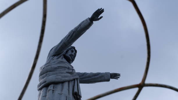 A low-angle view of a stone statue of Jesus Christ with upraised arms against a clear blue sky.