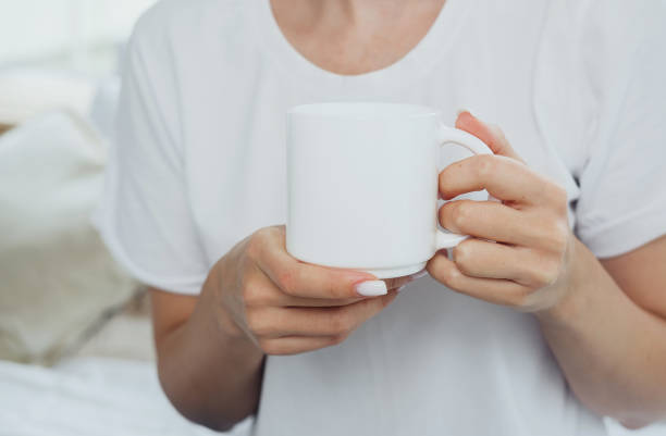 Young woman drinking tea or coffee holding a white cup with both hands while relaxing in a rocking chair. White mug mockup. The concept of rest on the weekend, on vacation.