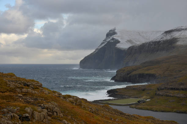 Aerial view of a soccer field surrounded by lake and ocean with snowcovered mountainrange just outside the small village of Eidi on the north-west tip of Eysturoy on Faroe Islands.