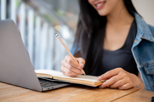 istock A close-up of a woman taking notes in a book while working remotely on her laptop at a coffee shop. 2181640728