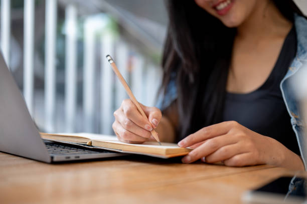 istock A close-up of a woman taking notes in a book while working remotely on her laptop at a coffee shop. 2181640733