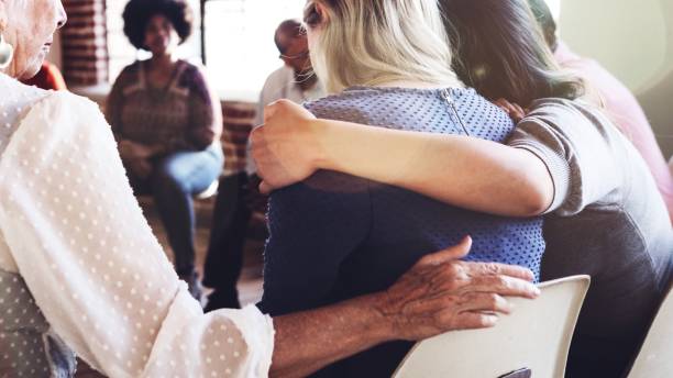 istock Support group meeting with diverse individuals sitting in a circle hugging and supporting one another. 2181646617