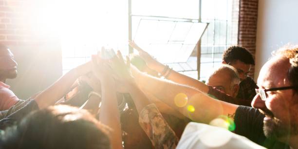 istock Diverse group of people joining hands upwards in sunlight, symbolizing teamwork and unity. 2181646660