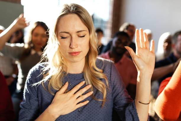 istock A person with closed eyes and raised hand in a group setting, expressing emotion. 2181646732