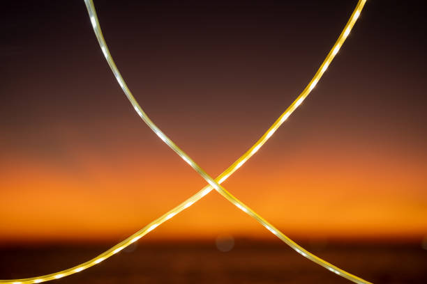 Two intertwined LED light strips glow against a vibrant orange sunset sky, creating a captivating silhouette. Perfect for themes of modern technology, decoration, and evening ambiance.