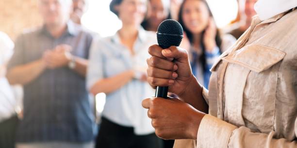 istock Woman in hijab holding a microphone in public with microphone, surrounded by diverse crowd. 2181649847