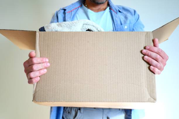 A man holds a cardboard box with clothes inside.