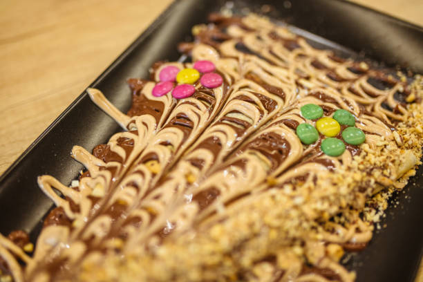 A beautifully crafted crepes featuring chocolate drizzle and colorful candy toppings on a black plate.