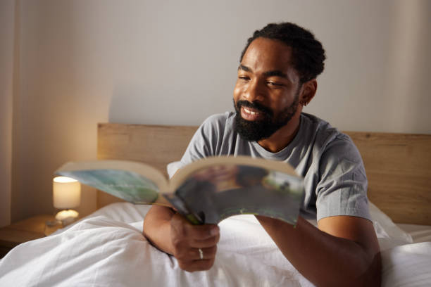 istock Happy black man reading a book in bed. 2181667079