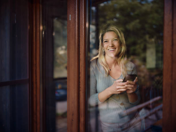 istock Happy woman using mobile phone by the window at home. 2181668540