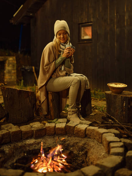 istock Smiling woman drinking tea during the night by the bonfire. 2181668645