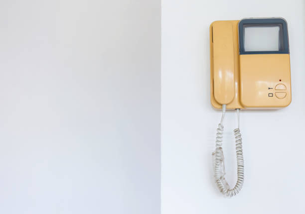 internal intercom with a handset for conversation and a video surveillance screen in a white body is suspended on the wall, closeup of a home security and communication device with copy space.