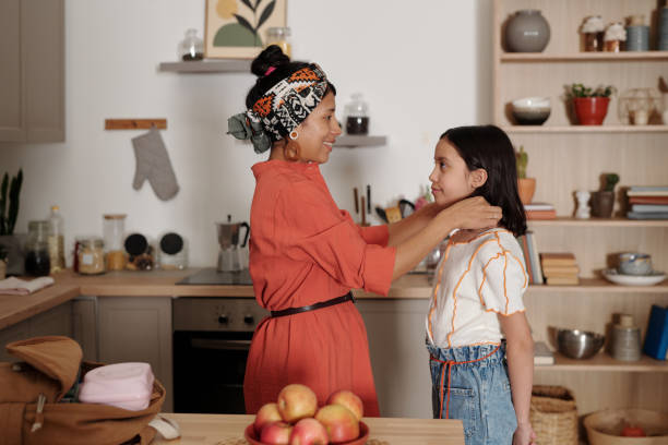 istock Smiling Woman Adjusting Child's Shirt in a Modern Kitchen 2181683564