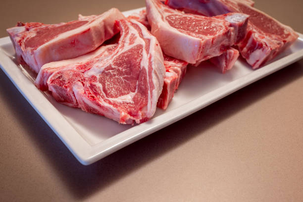 Several raw lamb chops placed on a white plate display fresh pink meat and fat layers The marbled texture emphasizes the quality of the lamb cuts prepared for cooking