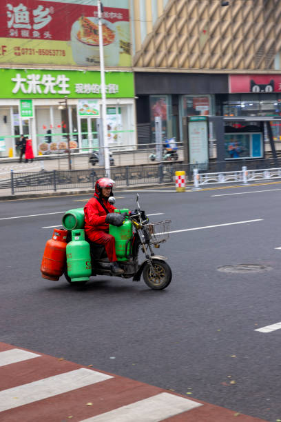 Changsha, China - 27 Feb 2024: A gas delivery worker in red attire rides a loaded motorcycle across the streets of Changsha, providing essential services to the city.