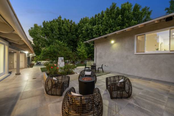 istock Modern backyard patio with wicker chairs and fire pit, surrounded by lush greenery 2181696842
